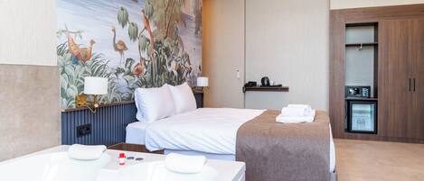 A hotel room with a large mural, a double bed, a separate bed, a bathtub, and a minibar.