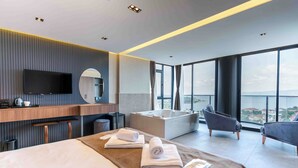 A modern hotel room with a large bed, a sitting area with a view, a bathtub, and a flat-screen TV.
