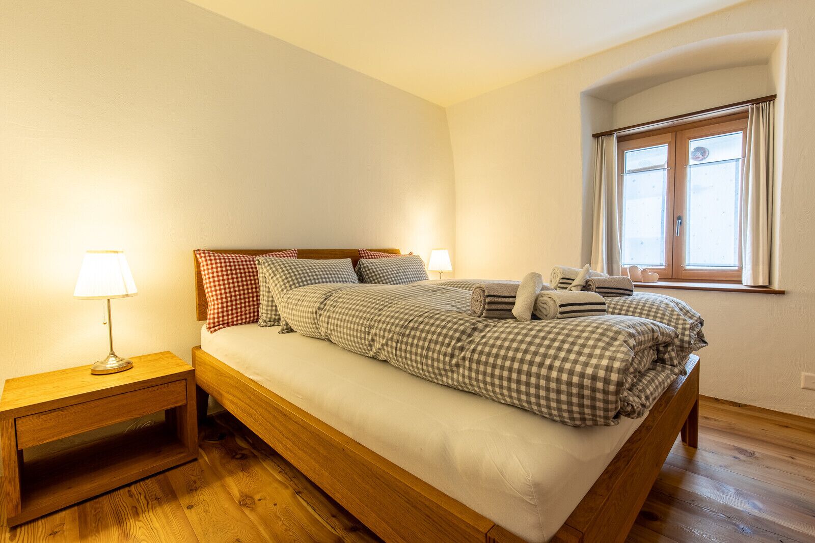 Un lit bien fait, avec une literie à carreaux, une lampe de chevet et une table de nuit en bois.