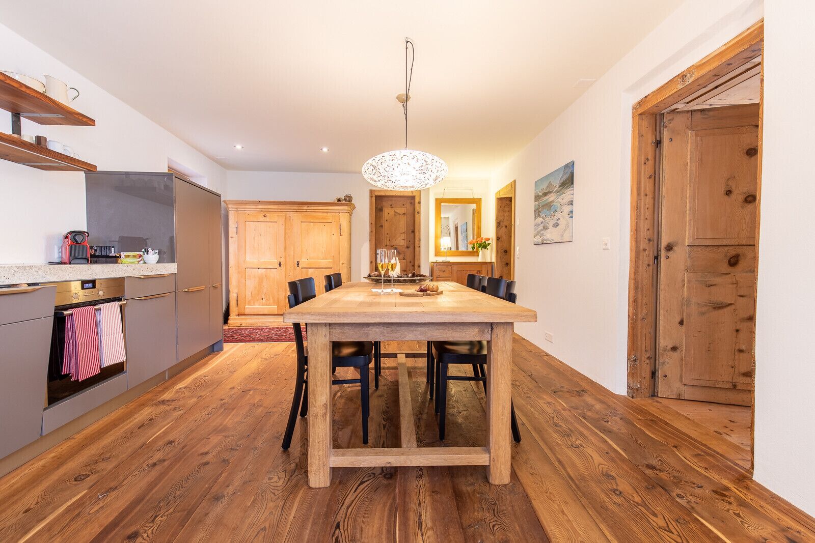 Un comedor con mesa y sillas de madera, una cocina con electrodomésticos modernos y una puerta de madera.