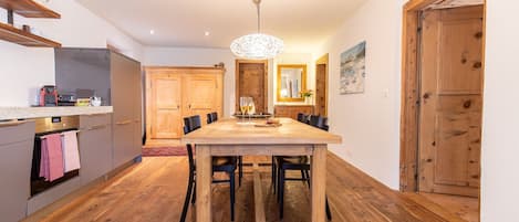 Un comedor con mesa y sillas de madera, una cocina con electrodomésticos modernos y una puerta de madera.