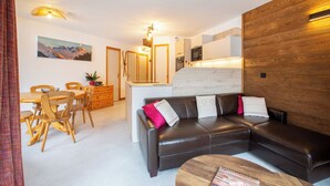 A modern living room with a leather sofa, wooden dining table, and chairs. There is a kitchen area with a microwave and a wooden wall. - Simply Morzine - Apartment le Sautaillet (Morzine)