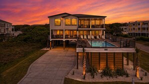 Una casa de dos pisos con piscina, rodeada por una terraza y un porche cubierto.