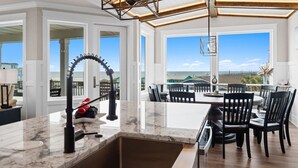 Una cocina moderna con una isla grande, un comedor con sillas y ventanas amplias con vistas.