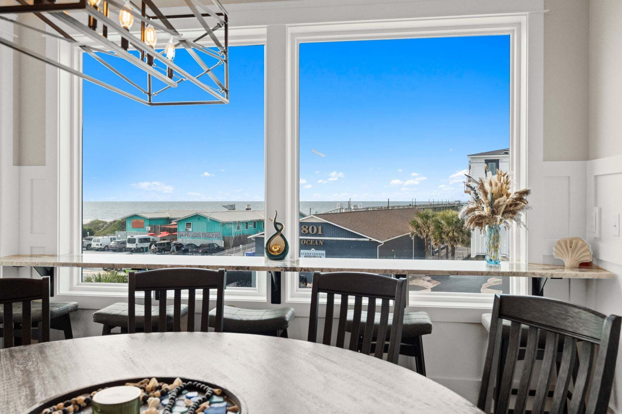 A dining area with a large window, wooden chairs, a table, and a decorative vase.