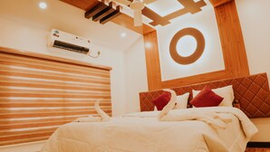 A hotel room with a bed, wooden ceiling beams, an air conditioning unit, and a circular light fixture.