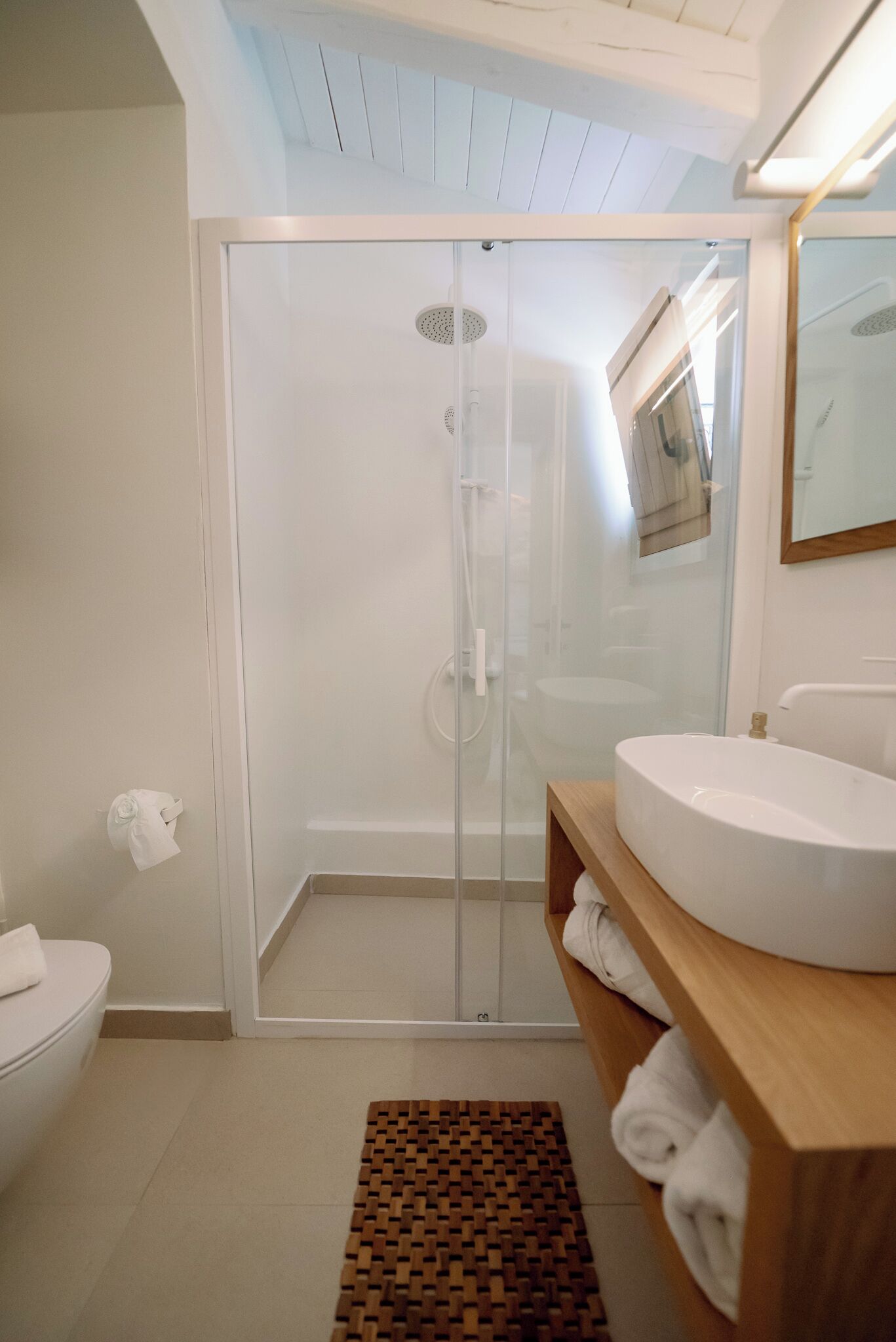 A modern bathroom with a glass shower enclosure, a white sink, and a wooden vanity.