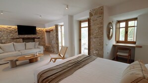 Una habitació d'hotel moderna amb un llit gran, un sofà, una taula de centre de fusta, un televisor fixat a una paret de pedra i un escriptori amb una cadira.