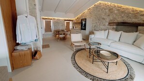 Un espai de vida ampli amb una paret de pedra, un sofà blanc, una taula de centre rodona i una zona de menjador amb mobiliari de fusta.