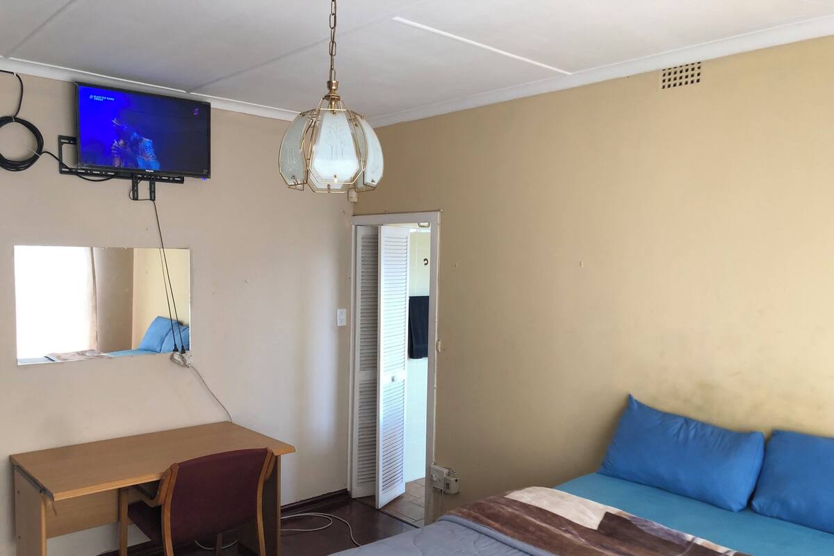 A room with a bed, a desk, a chair, a television mounted on the wall, and a door.