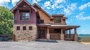 A two-story log cabin with a stone foundation, large windows, and a porch.