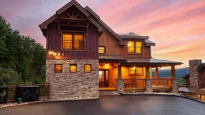 A large, two-story wooden house with a stone foundation, a porch, and a driveway.