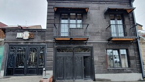 Un edificio de dos pisos con el letrero de un hotel boutique, grandes puertas dobles negras y un balcón con una viga de madera.