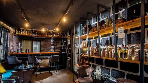 Zona de bar con asientos, estanterías llenas de botellas y pared de ladrillo.