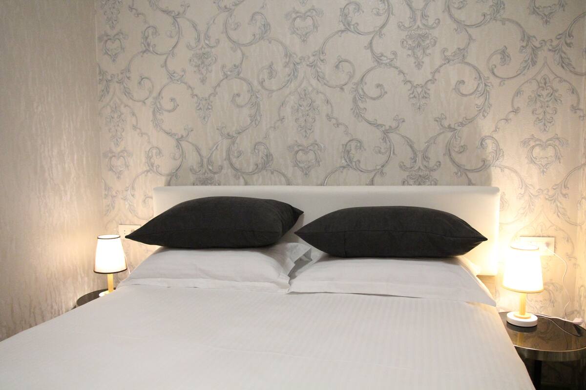A neatly made bed with white linens and two black pillows, flanked by two bedside lamps on matching nightstands.