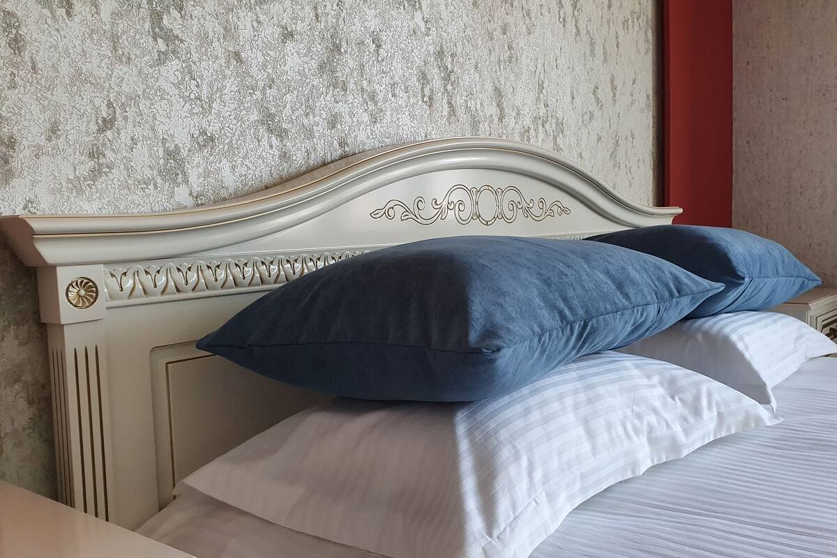 A bed with a white headboard and decorative carvings, accompanied by blue and white pillows.