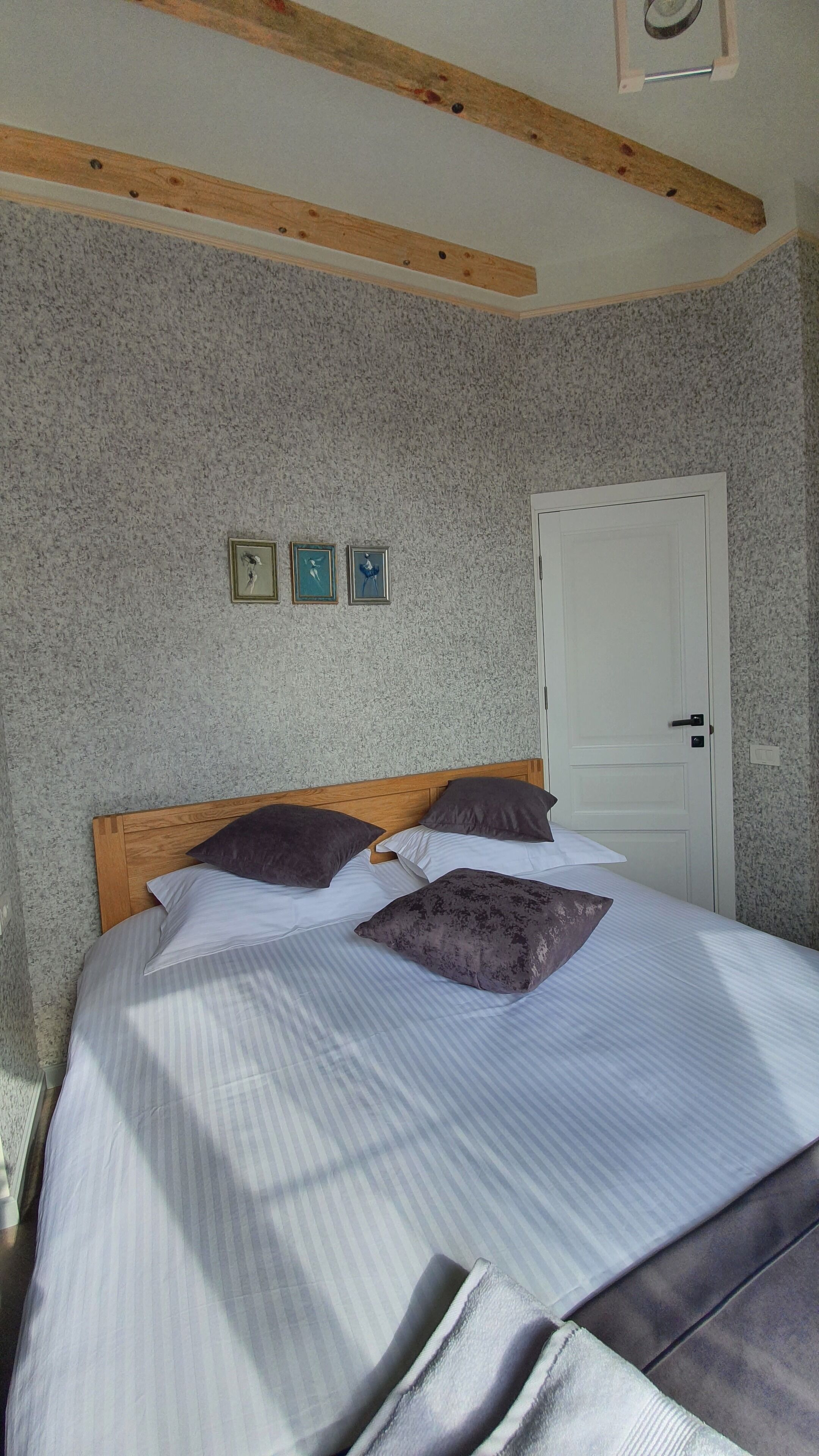 Un dormitorio con cabecera de madera, una cama con ropa de cama a rayas y tres cuadros en la pared.