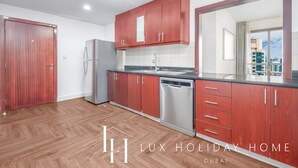 A modern kitchen with wooden cabinets, stainless steel appliances, and a large window offering a city view. - LUX The JBR Central Suite (Dubai)
