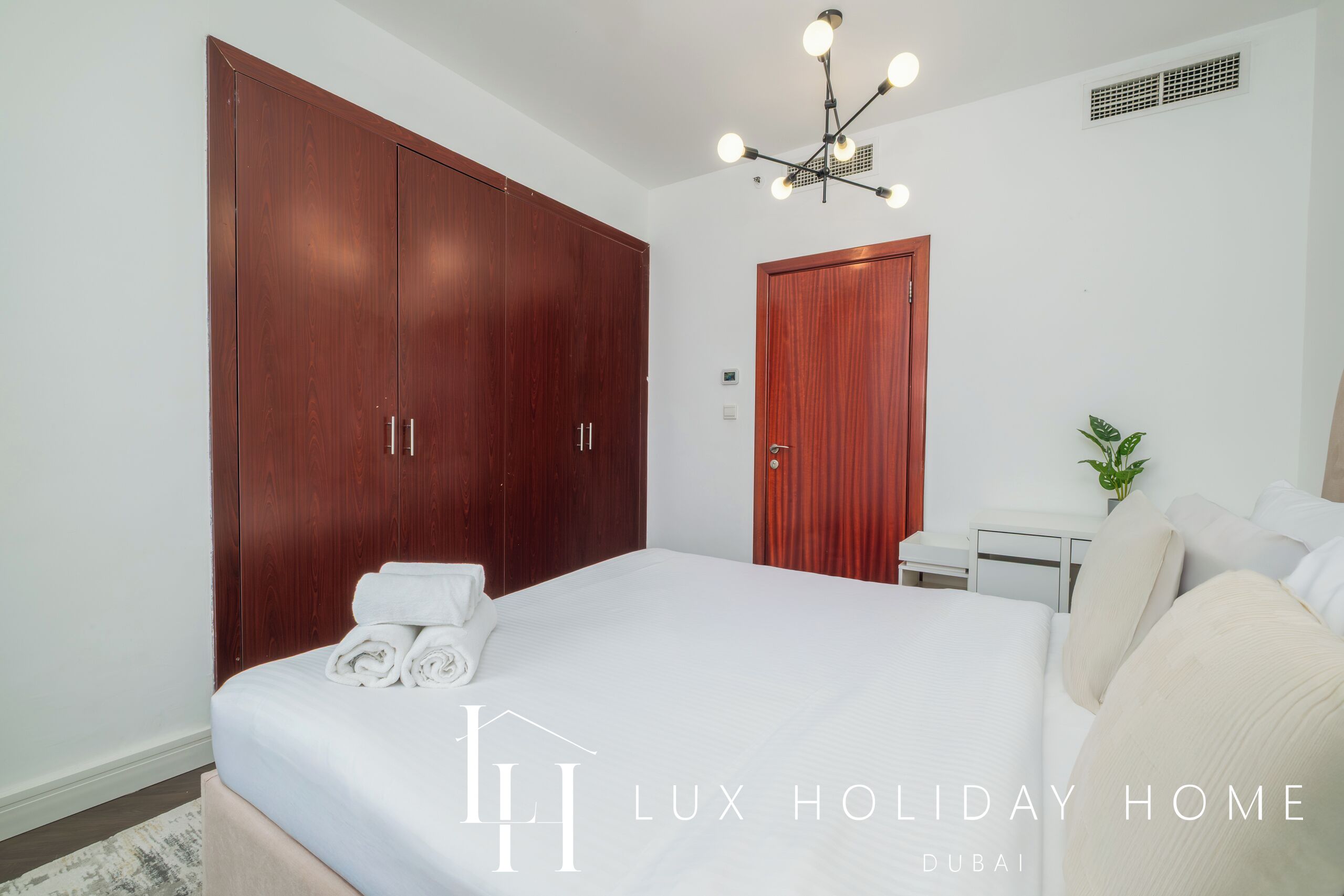 A hotel room with a large bed, wooden wardrobe, bedside table, and a ceiling light fixture.