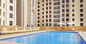 Una piscina con sillas de descanso y sombrillas, rodeada de edificios altos.