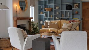 Un accogliente soggiorno con divano, poltrone, tavolino da caffè e libreria piena di oggetti decorativi.