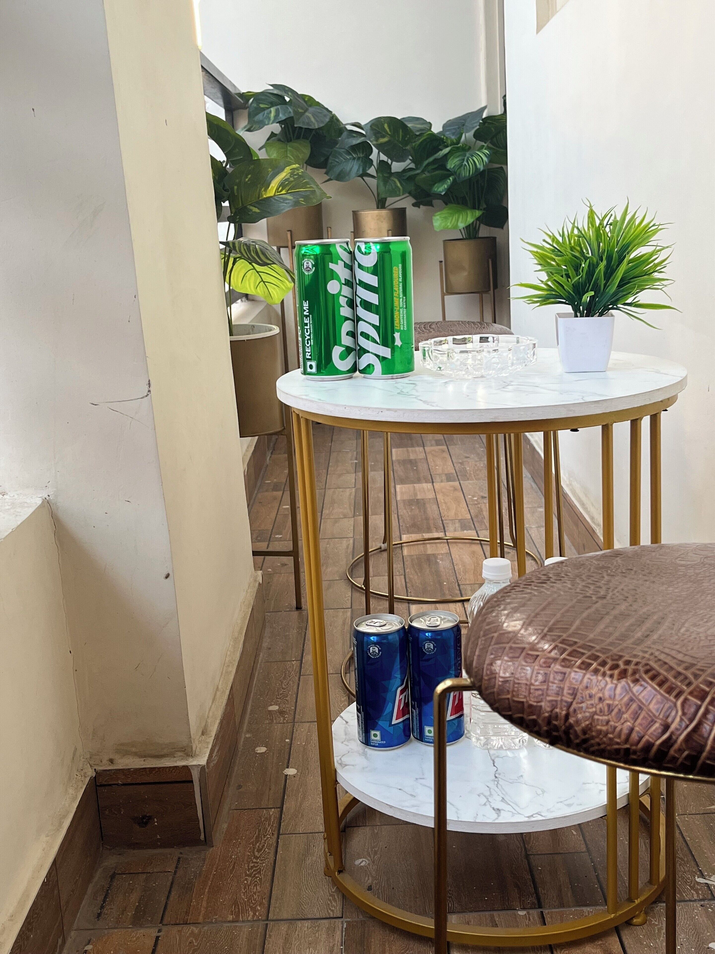 A round table with a white marble top and gold legs, accompanied by two cans of Sprite and a potted plant.