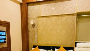 Une chambre d’hôtel avec un lit, une tête de lit en bois, un mur en marbre et un petit téléviseur fixé au mur.