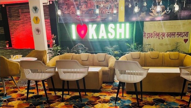 Un coin salon accueillant avec un canapé et des fauteuils, un sol coloré à motifs hexagonaux et un panneau néon sur lequel on peut lire : « J’♥ KASHI ».