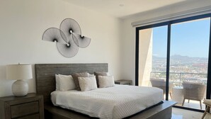 Un dormitorio moderno con una cama grande, una mesita de noche, una obra de arte en la pared y un balcón con vista a la ciudad.