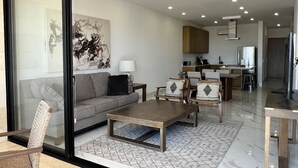 Una sala de estar moderna con un sofá, una mesa de centro y sillas, un área de cocina con armarios y electrodomésticos, y un comedor con mesa y sillas.