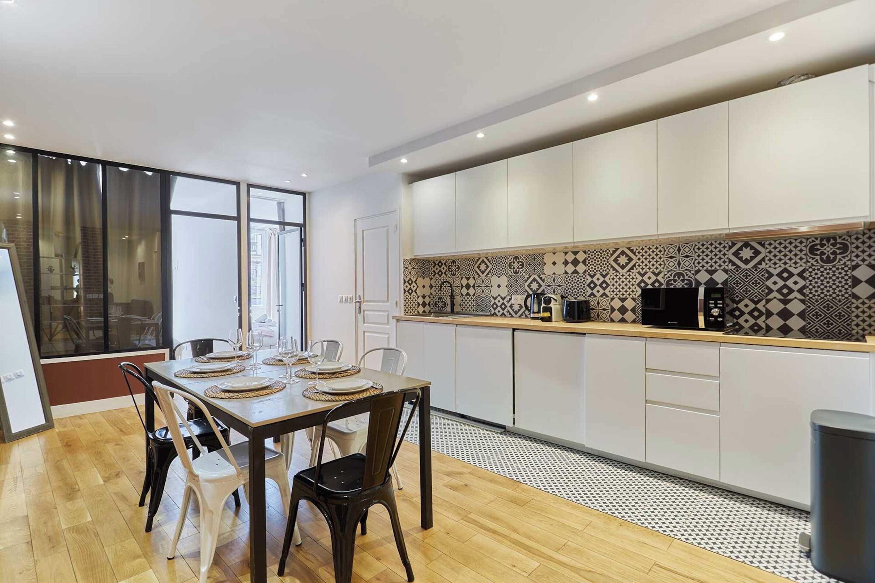 A modern kitchen with white cabinets, a patterned backsplash, and a dining area with a table set for four.