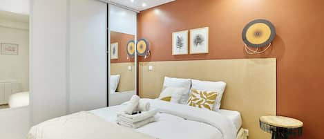 A modern bedroom with a large bed, a bedside table, and a wall-mounted mirror.
