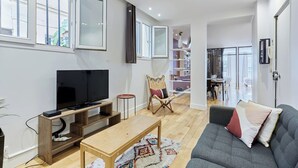 Una sala de estar moderna con televisor de pantalla plana, mueble de entretenimiento de madera, sofá gris y un comedor al fondo.