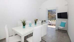 A white dining area with a table, chairs, potted plants, and a TV mounted on the wall. - VILLA DEI SRLS in Positano (Positano)