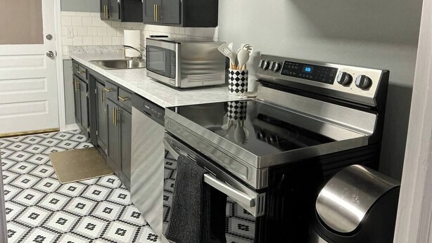 Uma cozinha moderna com armários escuros, micro-ondas, forno e coifa de aço inoxidável.