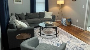 Uma sala de estar com sofá, mesa de centro, luminária e relógio na parede.