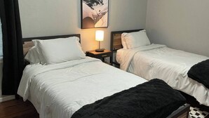 Quarto de hotel com duas camas de solteiro, uma mesa de cabeceira com abajur e um quadro na parede.