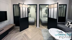 A modern hotel room with a large bed, a sofa, a TV, and a desk. There are two doors leading to a bathroom and a closet.