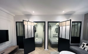 Una habitación de hotel moderna con una cama grande, un sofá, un televisor y un escritorio. Hay dos puertas que dan a un baño y a un armario.