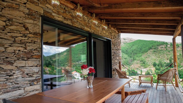 Une terrasse en bois avec un muret en pierre, une table avec des chaises et un vase rempli de fleurs.