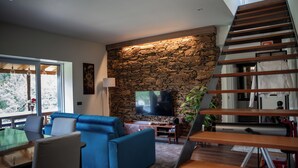Un salon moderne avec un mur en pierre, un canapé bleu, un escalier en bois et un téléviseur à écran plat.