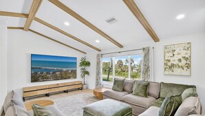 A modern living room with a large window, a sofa set, a wooden bench, and a painting on the wall. - Coastal retreat!   West end steps to beach! (Sanibel)