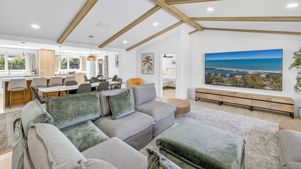 A spacious living area with a large gray sectional sofa, wooden beams on the ceiling, a dining area with modern furniture, and a large window with a view of the sea. - Coastal retreat!   West end steps to beach! (Sanibel)