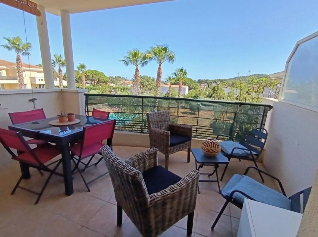 Un balcon avec une table et des chaises pour prendre les repas, un fauteuil en osier et une vue sur les palmiers et les immeubles.