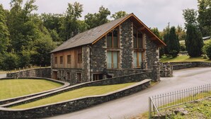 A stone building with a wooden exterior and a sloped roof, surrounded by a stone wall and a curved driveway.