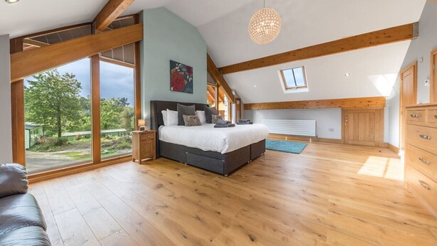 A spacious bedroom with a large bed, wooden beams, a view of the outdoors, and a skylight.