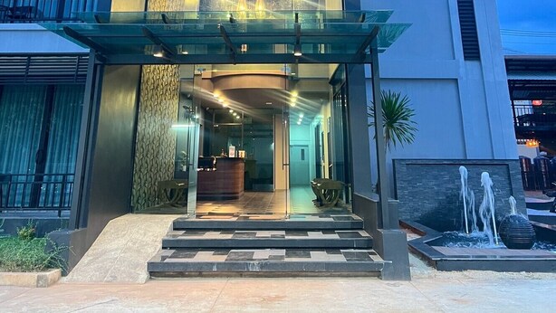 A modern hotel entrance with a glass facade, a reception desk, and a water feature outside. - HF Ville (Surat Thani)