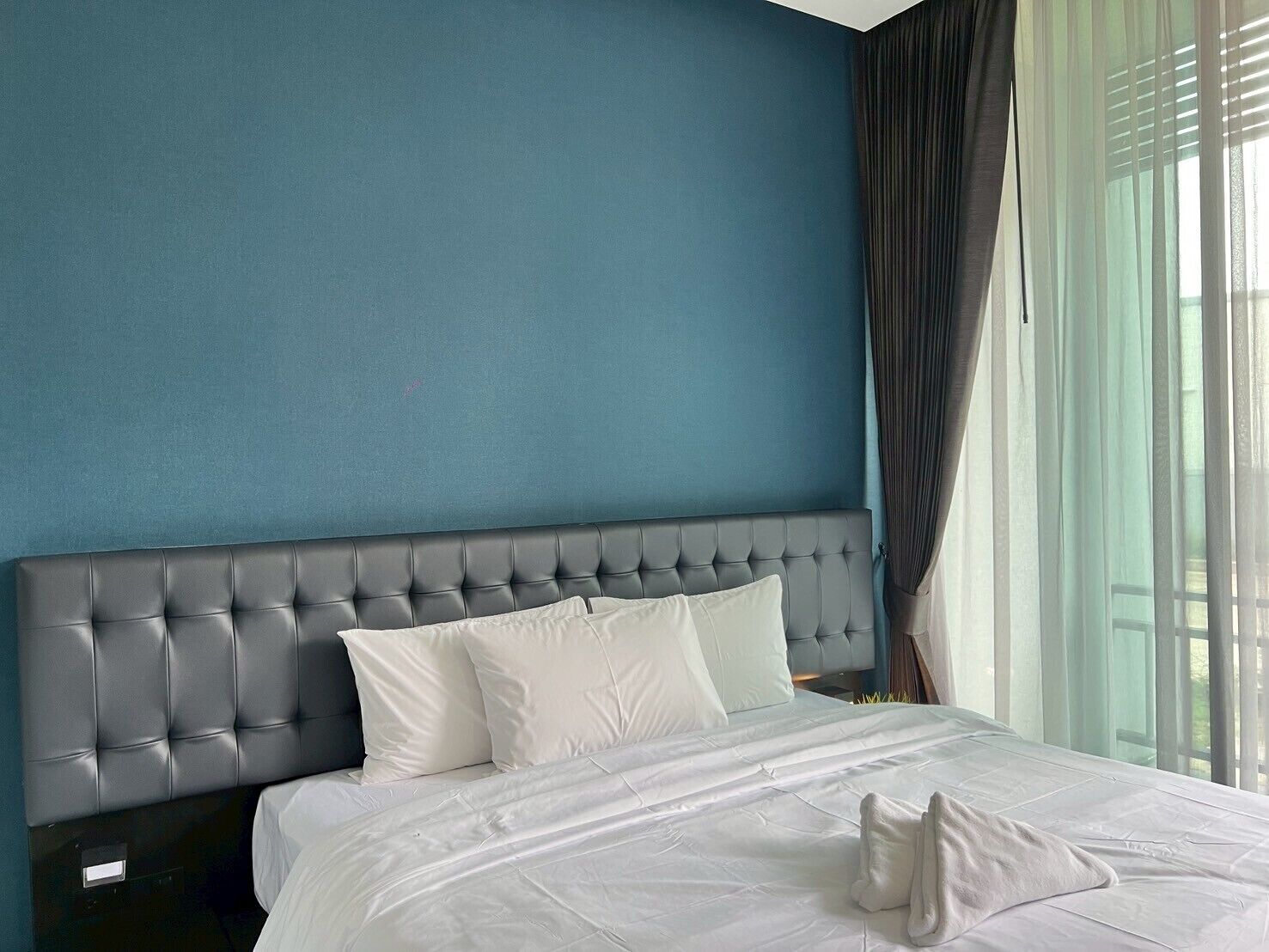 A hotel room with a large bed, a tufted headboard, and sheer curtains.