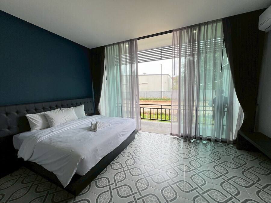 A hotel room with a large bed, a view of the outdoors through sheer curtains, and a patterned floor.