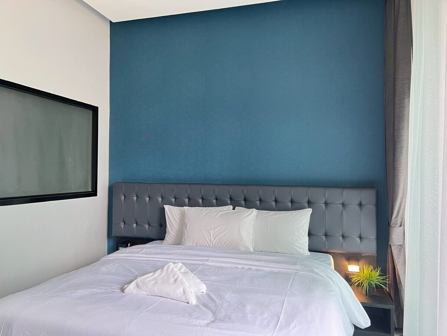 A neatly made bed with white linens and pillows, a grey tufted headboard, and a small bedside plant.